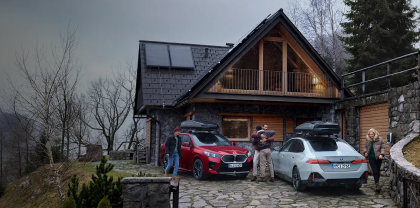 Zwei autos mit Dachkoffer vor einem Haus. Vier Personen begrüßen sich.